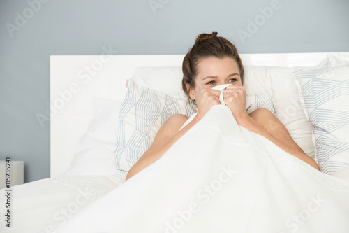 Young woman sitting up in bed hiding