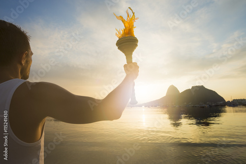 Torchbearer athlete standing with sport torch against a scenic sunrise view of Sugarloaf Mountain and Botafogo Bay in Rio de Janeiro, Brazil photo