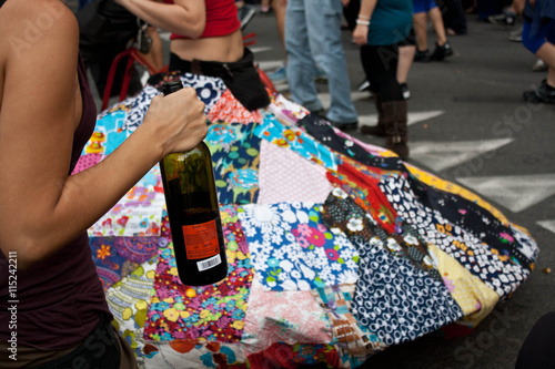 Braccio che tiene in mano una bottiglia di vino e sullo sfondo una gonna enorme e coloratissima photo