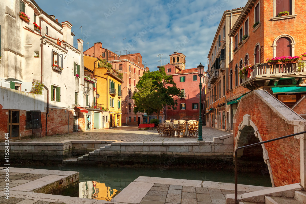 Colorful narrow lateral canal, square and pedestrian bridge in Venice, Italy