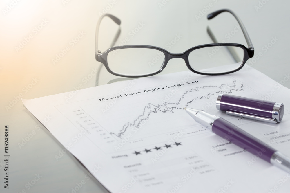 Mutual Fund information with performance line graph and benchmark with pen and glasses. Mutual Fund information with performance line graph and benchmark with pen and glasses.