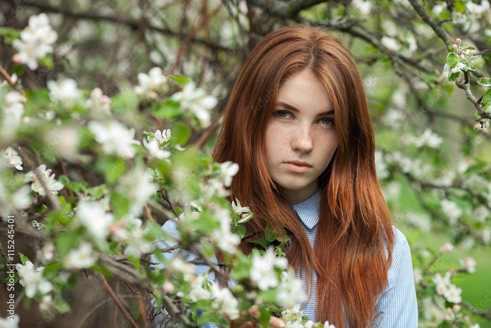 Portrait of a beautiful redhead women in shirt and jeans in blossom apple tree garden in spring time Portrait of a beautiful redhead women in shirt and jeans in blossom apple tree garden in spring time