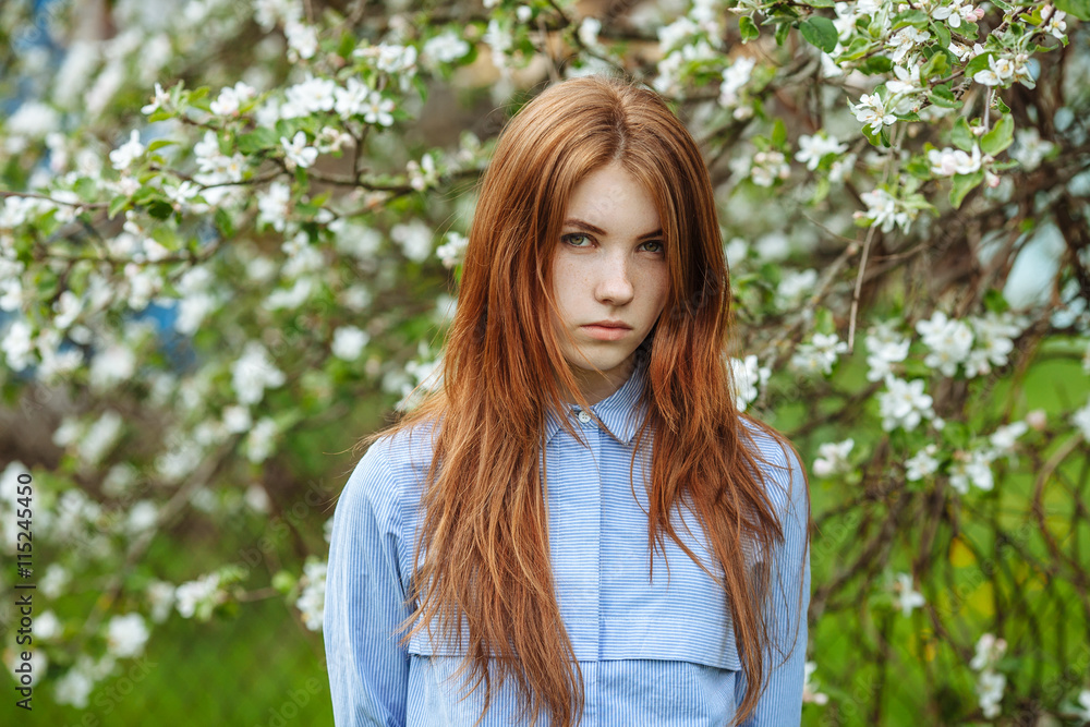 Portrait of a serious beautiful redhead women in shirt and jeans in blossom apple tree garden in spring time Portrait of a serious beautiful redhead women in shirt and jeans in blossom apple tree garden in spring time