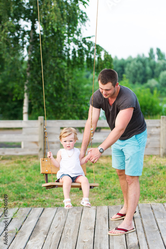 Father with his adorable baby daughter playing swing in the garden.