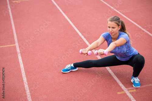 Young female stretching with weight on a racing track