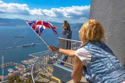 Tourist woman holding an English flag observes one of the famous monkeys of Gibraltar from the top of Gibraltar Rock, in the Upper Rock Natural Reserve.