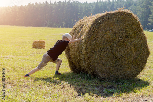 Fényképezés A boy pushes a large haystack.Toning