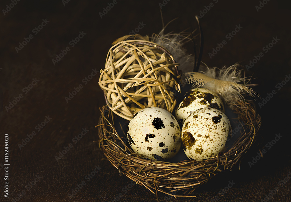 Obraz premium quail eggs in a small nest with a decorative element - a ball of straw on a dark background