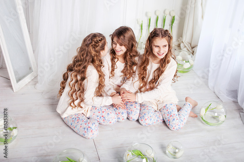 Three pretty little girls sit on a floorand whisper each other photo