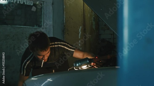 Car mechanic with a cigarette in his mouth fixing a car in the garage, wide angle photo