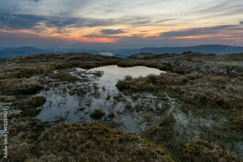 Vibrant orange sunrise with boggy water from Place Fell in the English Lake District.