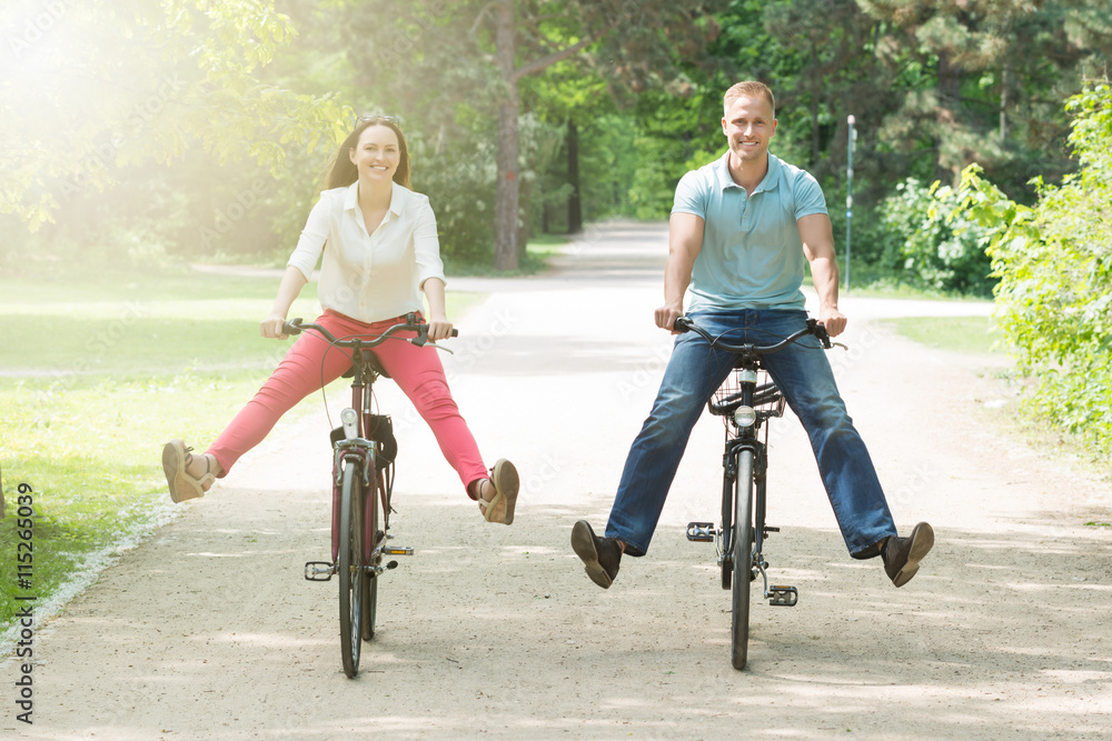 Happy Couple Riding Bicycle In Park - obrazy, fototapety, plakaty 
