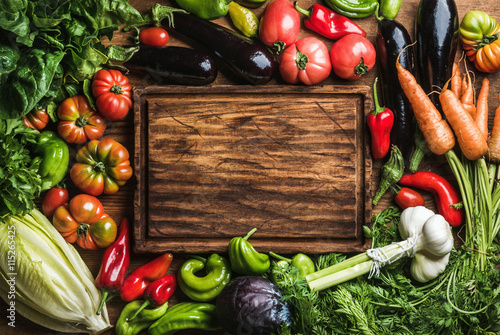 Fresh raw vegetable ingredients for healthy cooking or salad making with rustic wood board in center, top view, copy space photo