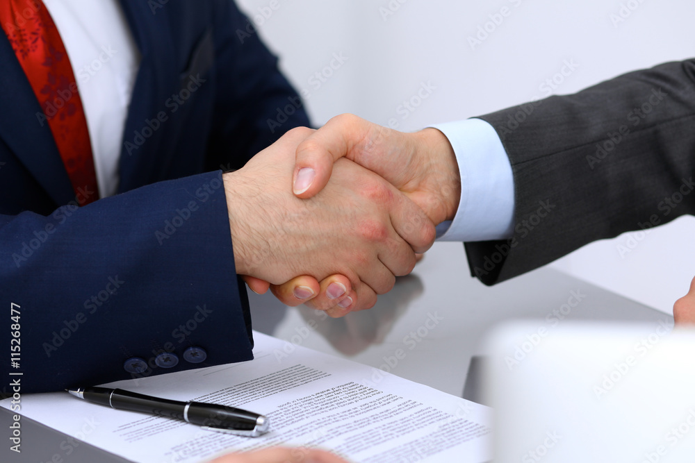 Two business man shaking hands to each other above signed contract Two business man shaking hands to each other above signed contract