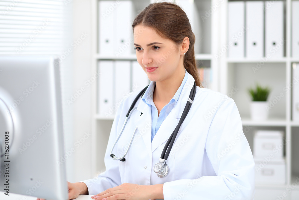 Young brunette female doctor sitting at the table and working at hospital office. Health care, insurance and help concept. Physician ready to examine patient Young brunette female doctor sitting at the table and working at hospital office. Health care, insurance and help concept. Physician ready to examine patient
