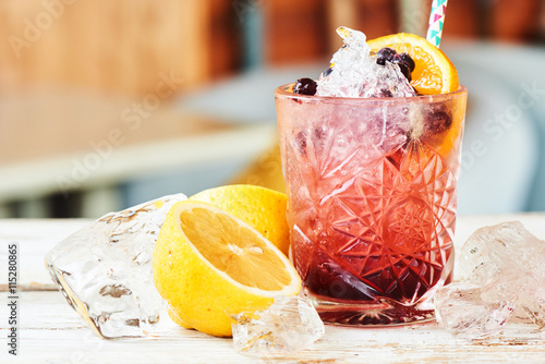 Alcoholic cocktail consisting of currants, blackberries, and liqueur in a glass and lemon on a wooden table