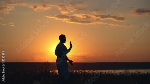 Silhouette of man training karate at sunset.