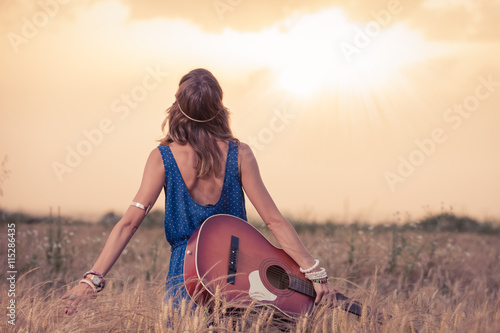 Photo Young retro hippy styled woman with acoustic guitar in wheat field looking at sun to find inspiration for the next song