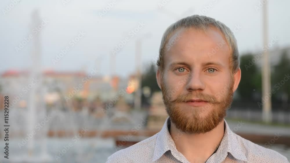 blond man with blue eyes and beard near the fountain looking at the camera blond man with blue eyes and beard near the fountain looking at the camera