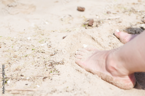 Feet of a woman with white nails on a beach sand in a sun.