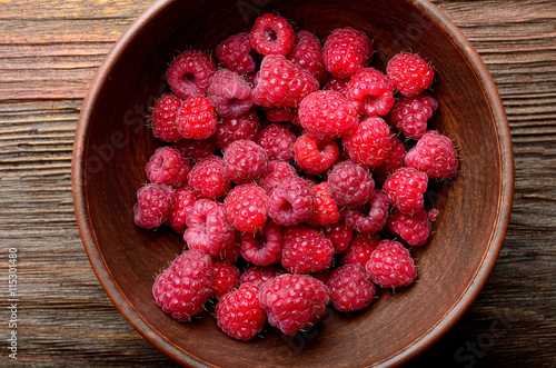 raspberries in a clay bowl on a wooden table