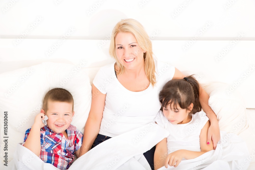A mother relaxing in bed with her daughter and her son..