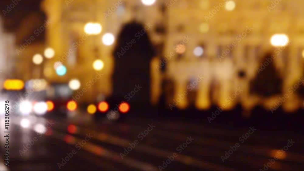Pedestrians walking in the center of Prague city street at night with light illumination, and traffic of cars and trams. Blurred defocused background. Pedestrians walking in the center of Prague city street at night with light illumination, and traffic of cars and trams. Blurred defocused background.