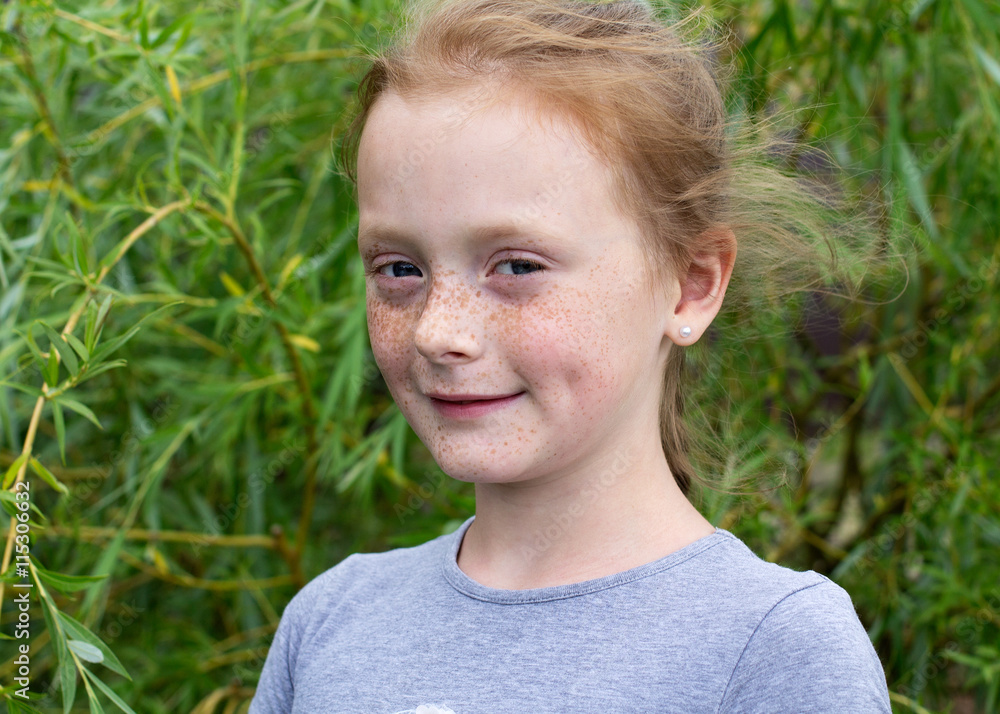Close up portrait of a ginger smiling girl with freckles against green leaves Close up portrait of a ginger smiling girl with freckles against green leaves