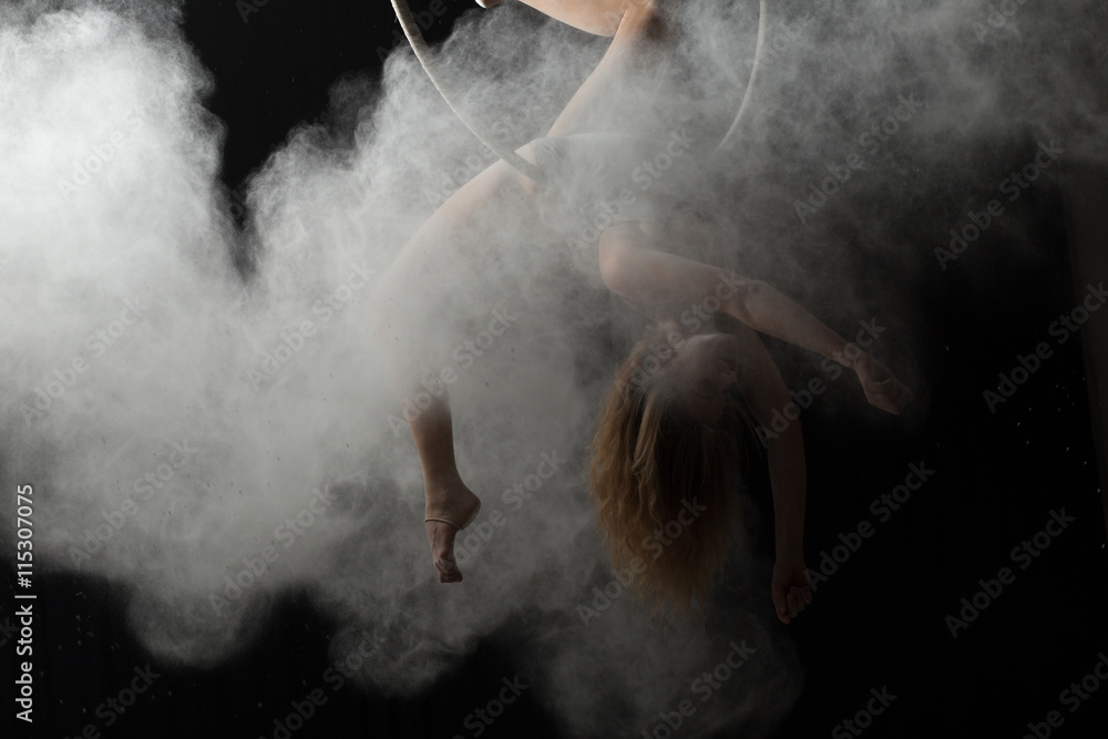 Obraz premium Acrobatic woman doing gymnastic element on aerial hoop with sprinkled flour
