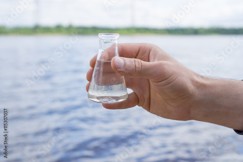 Hand holding a chemical flask with water, lake or river in the background. photo