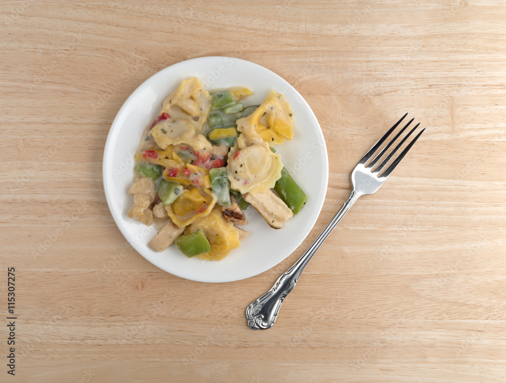 Chicken and tortellini TV dinner on plate with a fork to the side atop a wood table. Chicken and tortellini TV dinner on plate with a fork to the side atop a wood table.