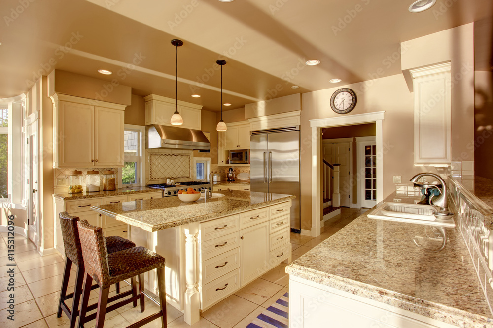 Large luxury kitchen room in beige colors with granite counter tops and tile floor.
