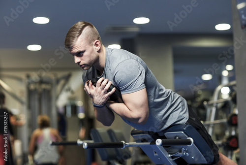 Fototapeta Naklejka Na Ścianę i Meble -  young man flexing back muscles on bench in gym