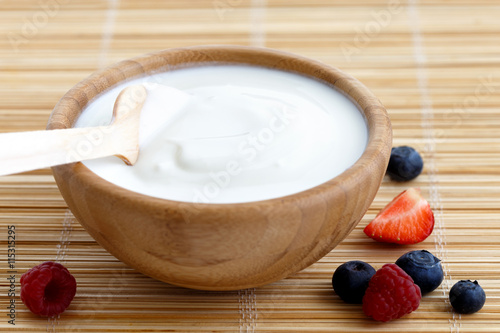 Wooden bowl of white yoghurt with wooden spoon.
