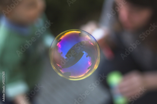 Soap bubble reflecting sunset colors and woman with little kid in the background.