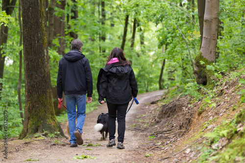 Canvas Print Middle aged couple walking their two dogs in forest.