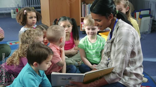 Students interacting with their teacher during storytime at nursery. They are sitting on the floor in the classroom.