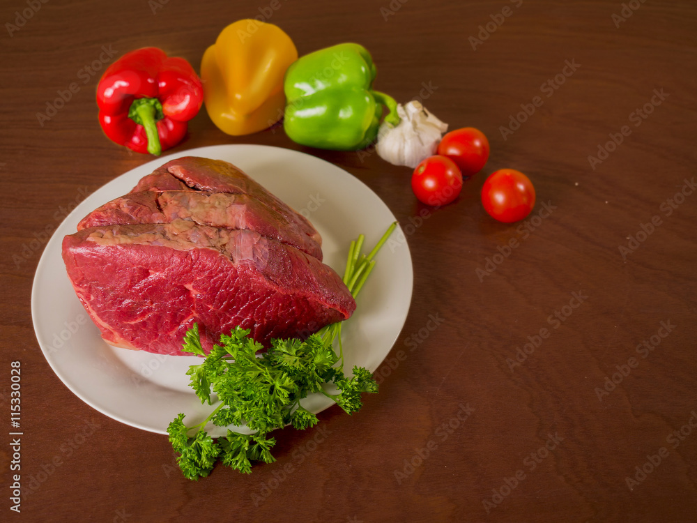 Raw beef joint on a plate and some vegetables. Raw beef joint on a plate and some vegetables.