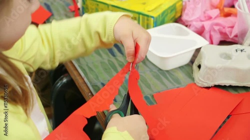 Little girl aty nursery cutting some red paper with scissors. photo