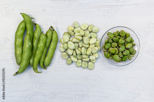 Broad beans in triple form : pods, podded beans and cooked beans on a white table, top view