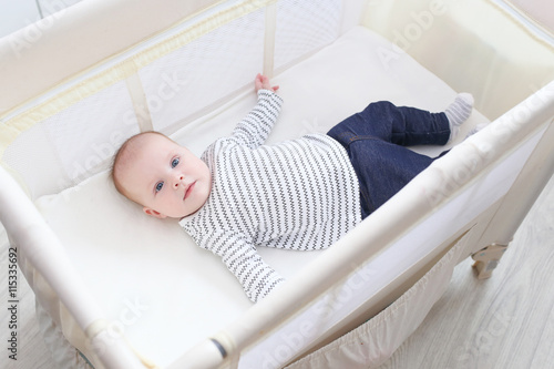 Lovely little 3 months baby lying in travel crib