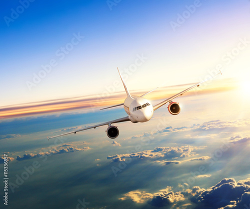 Airplane flying above clouds in dramatic sunset