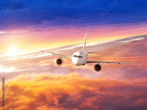 Airplane flying above clouds in dramatic sunset