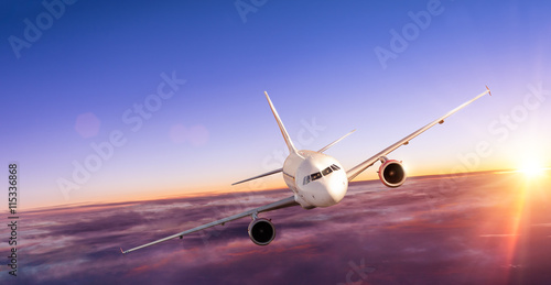 Fotografie Airplane flying above clouds in dramatic sunset