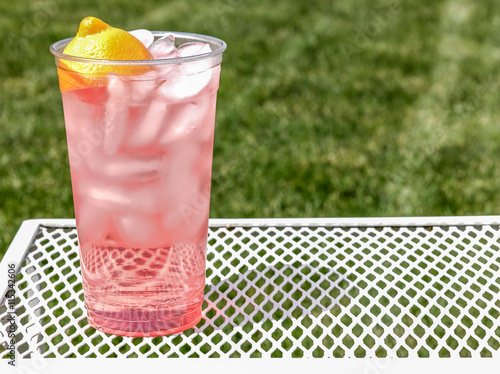Fresh Squeezed pink lemonade it a clear cup outside on a lawn table.