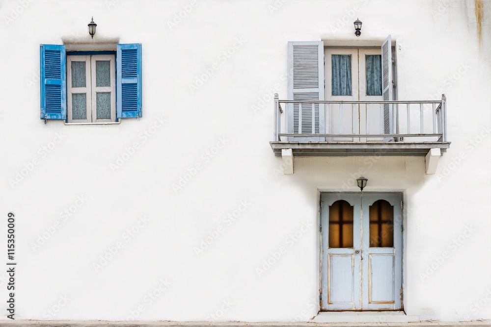The front of the house with a white wall with doors, windows and balconies.