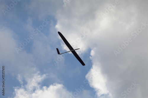 RC glider silhouette flying in the blue sky, white clouds background