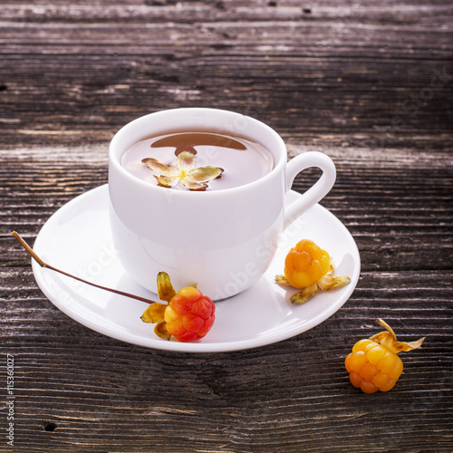Useful light breakfast snack. Fresh herbal fruit tea with berries and leaves north cloudberries in a white ceramic cup on  dark wooden background. Rare very  berry, called the king. photo