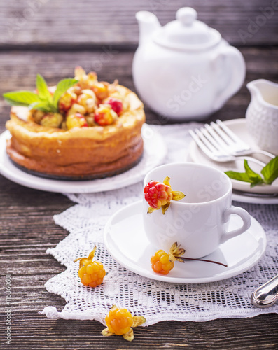 Homemade breakfast. Fresh cheesecake with berries ripe northern rare cloudberries on a wooden background vintage handmade embroidered tablecloth. Served white ceramic dishes