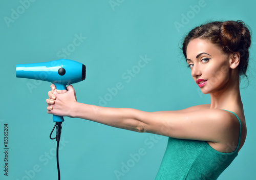 Happy young curly brunette woman with hair dryer on blue mint ba